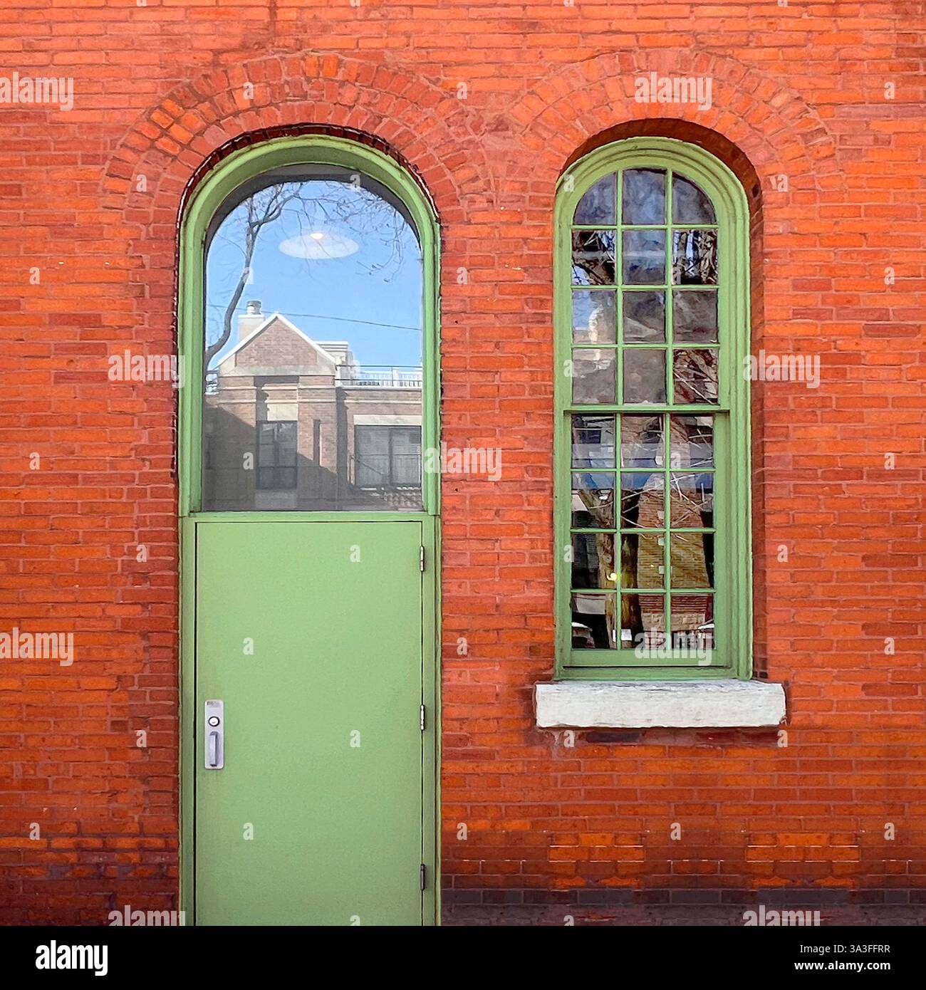 Rustic red brick facade with arched green door and window, reflecting urban architecture. - Smartphone Captured Stock Image