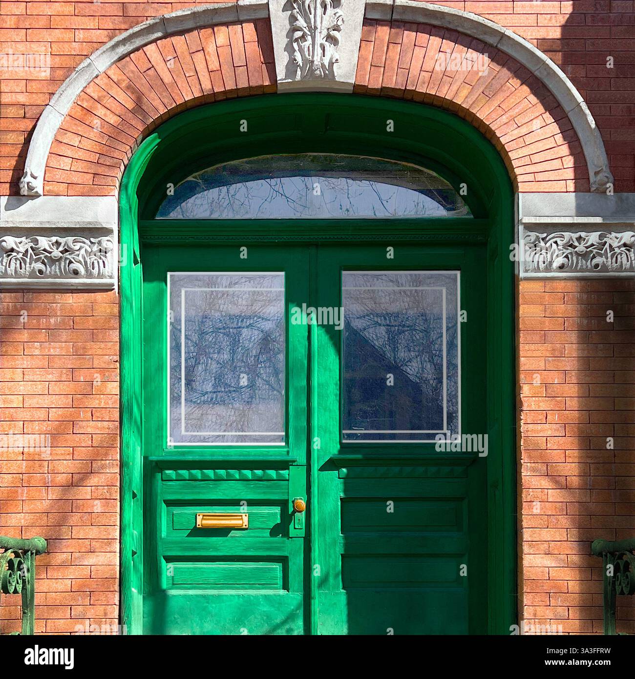 Green arched double doors set in a historic warm brick facade with ornate stone detailing. - Smartphone Captured Stock Image