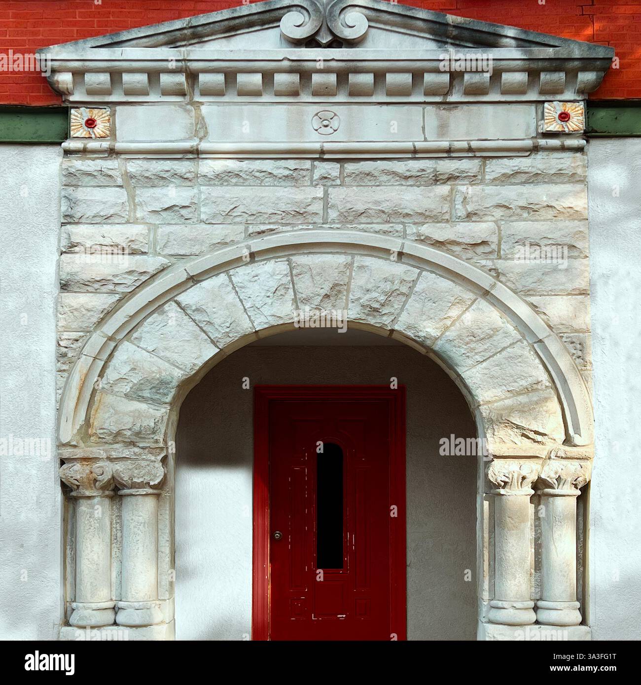 Red door framed by an ornate Romanesque stone archway with intricate column details, set against a historic brick and stucco facade. - Smartphone Captured Stock Image