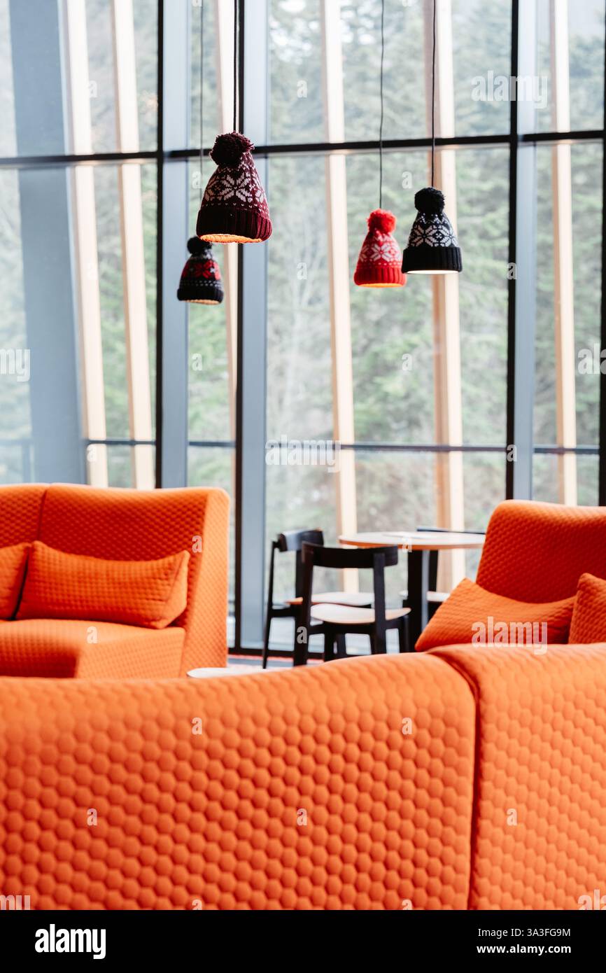 Stylish winter themed interior design with cozy orange furniture and playful beanie shaped lamps against a scenic window view Stock Photo