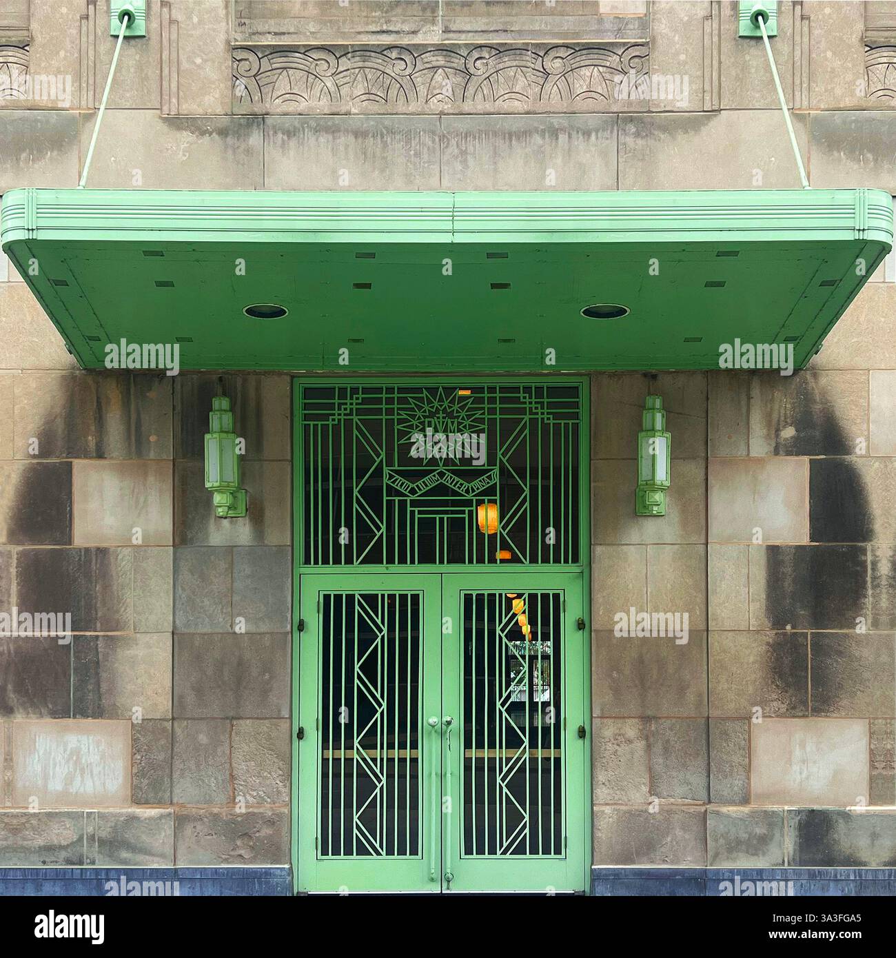 Art Deco entrance featuring an ornate mint-green metal door, geometric patterns, decorative ironwork, and matching overhead awning. - Smartphone Captured Stock Image