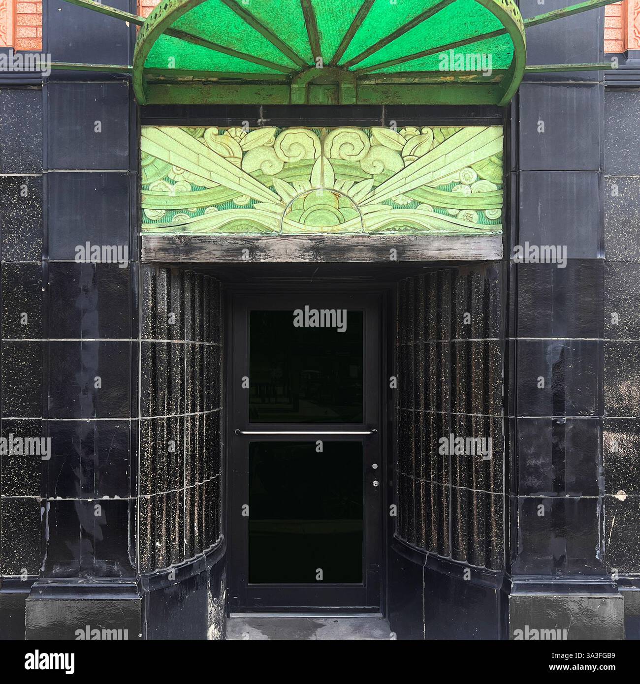 Historic Art Deco entrance featuring a green stained-glass awning and decorative terra cotta tilework above a sleek black doorway, Chicago. - Smartphone Captured Stock Image