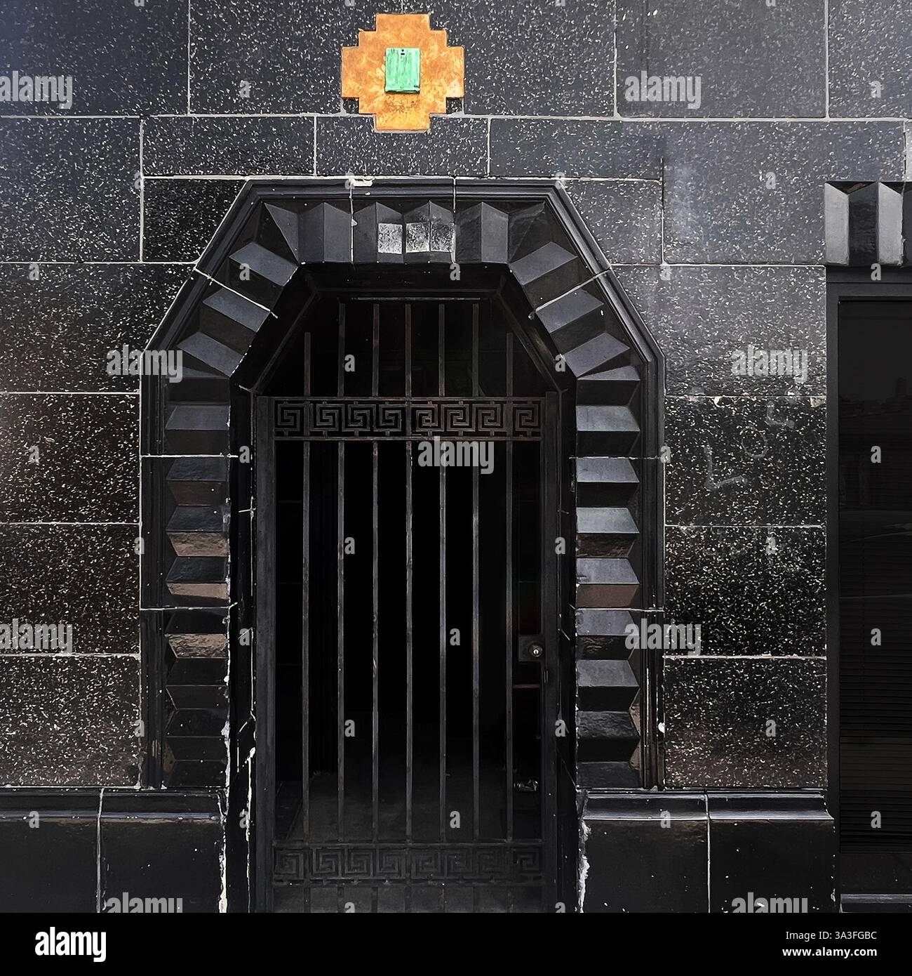 Art Deco entrance with striking black geometric tilework, metal gate, and decorative gold and green tile accent. - Smartphone Captured Stock Image