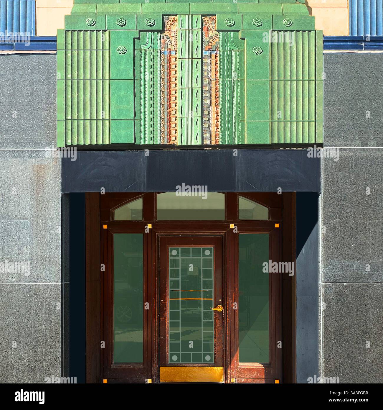 Art Deco entrance featuring ornate green terra cotta tilework, intricate geometric patterns, polished wood door, and brass accents on a vintage facade. - Smartphone Captured Stock Image