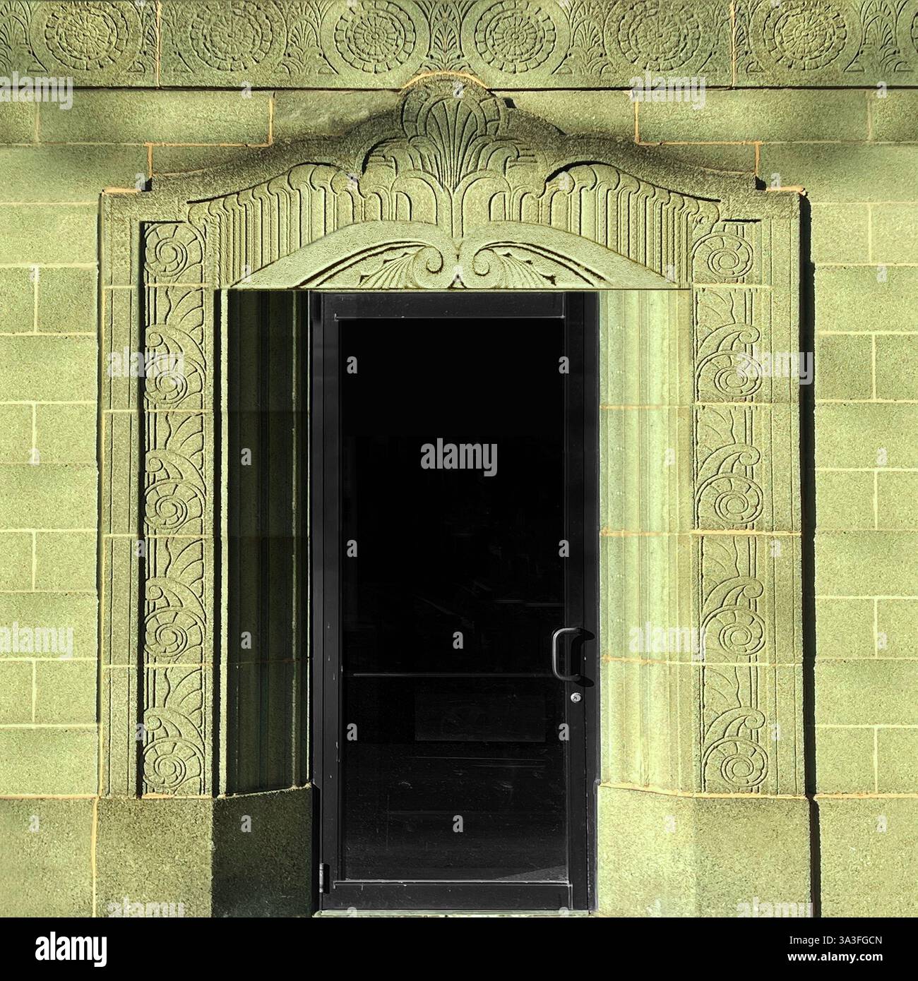 Art Deco doorway featuring detailed carvings on a green stone facade highlighted by intricate floral and geometric motifs. - Smartphone Captured Stock Image