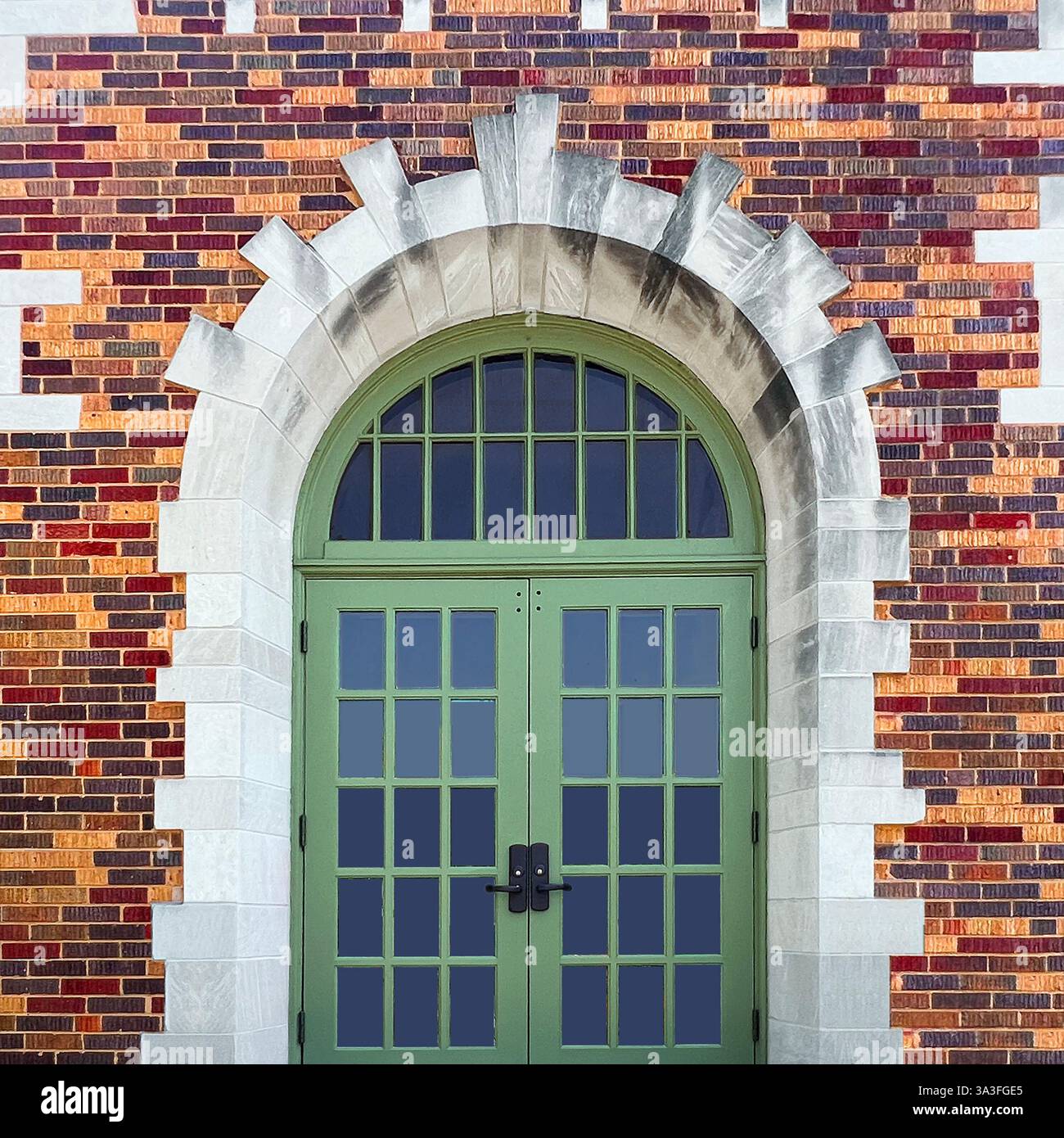 Arched green  doors with glass panels, set within a grand arched stone entrance, surrounded by colorful, detailed brickwork. - Smartphone Captured Stock Image