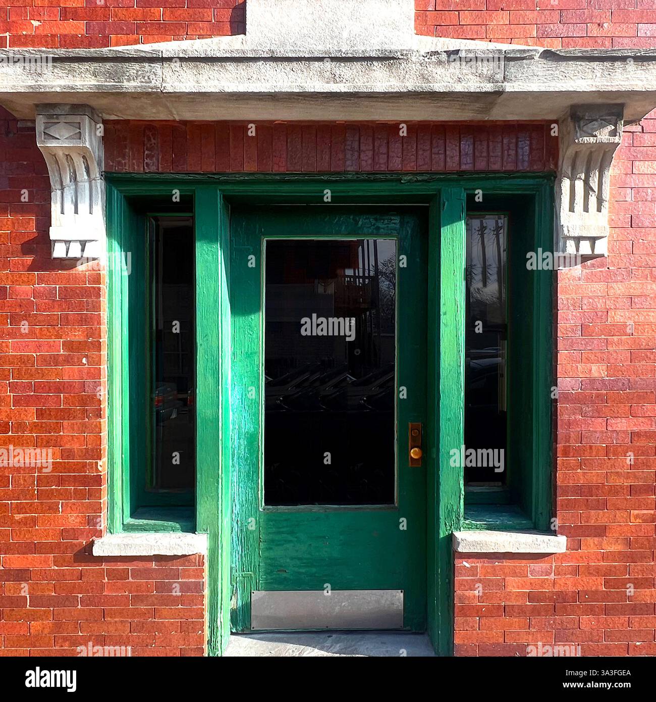 Vintage Green door with glass panel, framed by detailed stonework and red glazed brick facade. - Smartphone Captured Stock Image