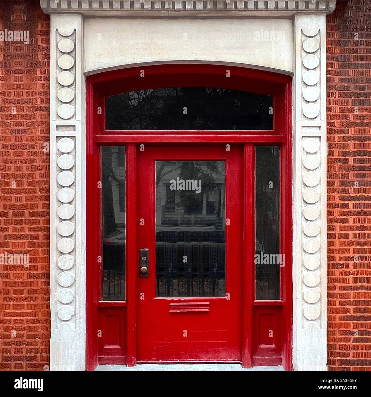 Historic urban doorway featuring a vibrant red wooden door with decorative glass panels, elegantly framed by detailed stone trim and brick facade. - Smartphone Captured Stock Image