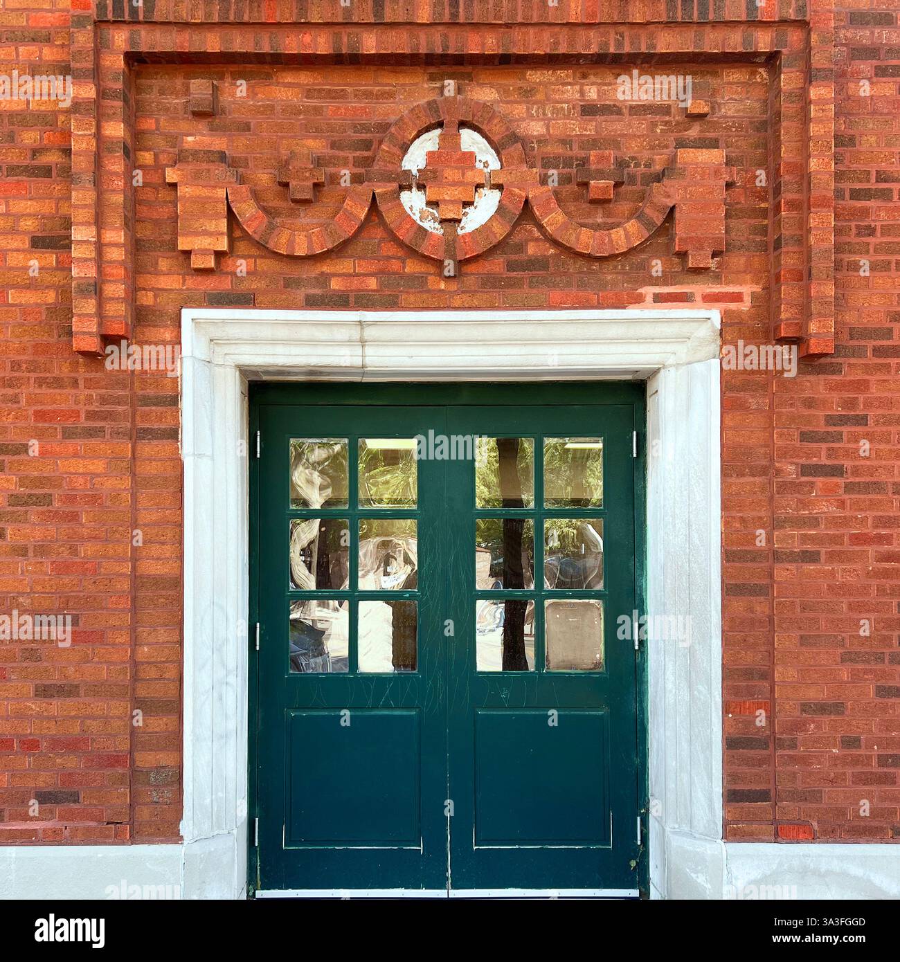 Dark green double doors with glass panes set in an ornate orange brick facade with decorative geometric brickwork and a white stone frame in Chicago. - Smartphone Captured Stock Image
