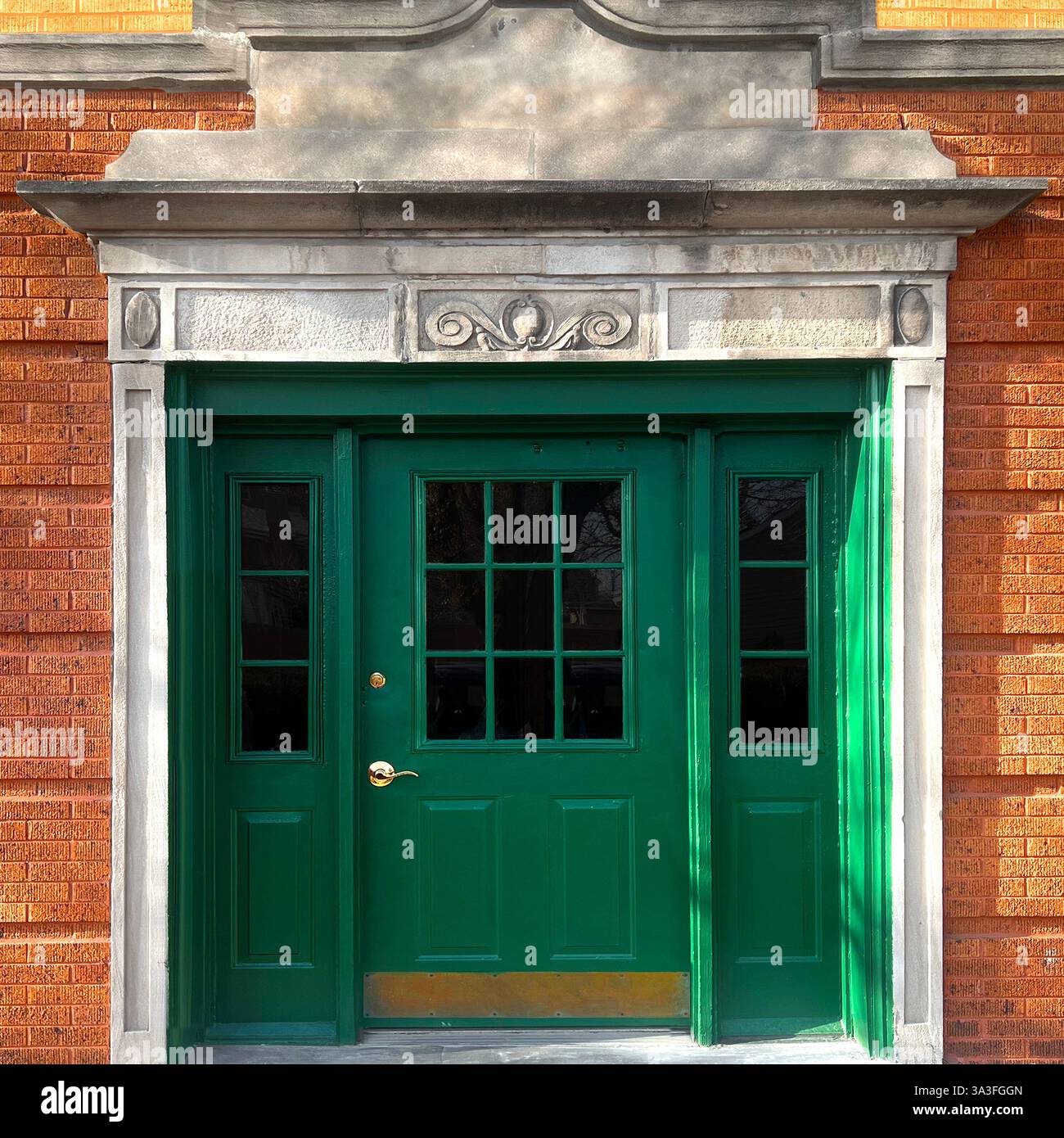 Bright green wooden entrance door with decorative glass panels aframed by ornate stone detailing and orange brick facade in Chicago. - Smartphone Captured Stock Image