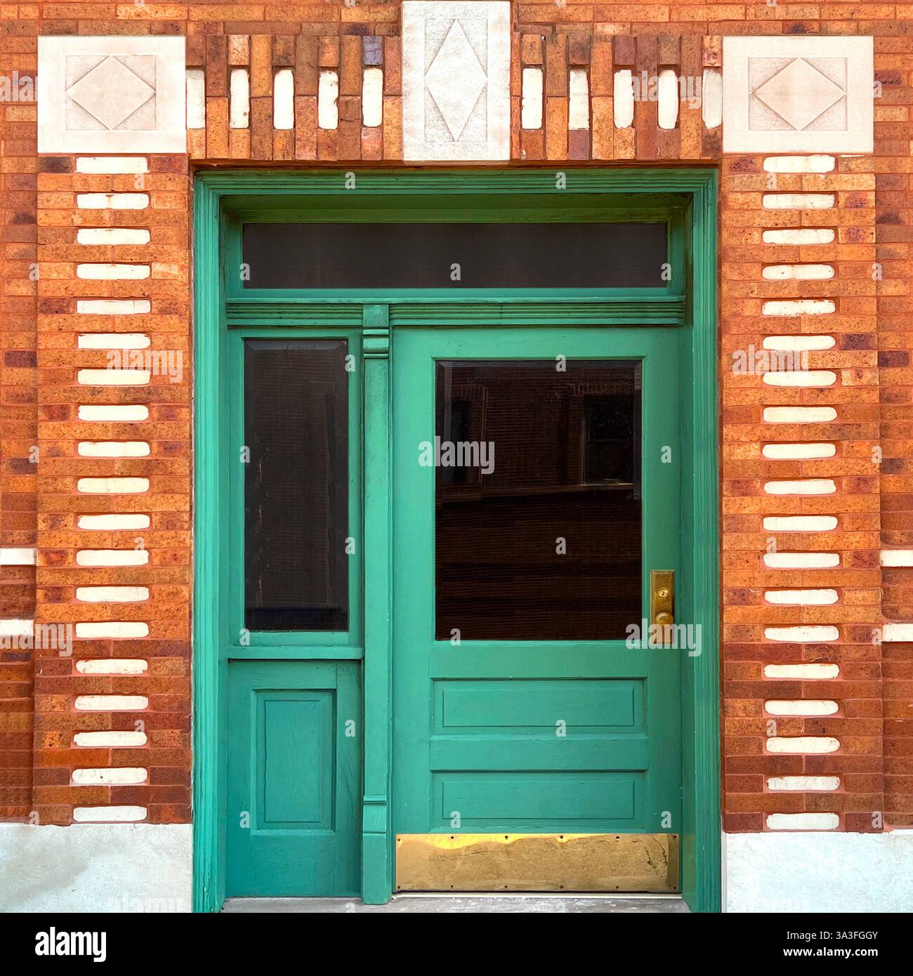 Green door with glass panels is set within an intricate brick-and-stone facade that features geometric patterns - Smartphone Captured Stock Image