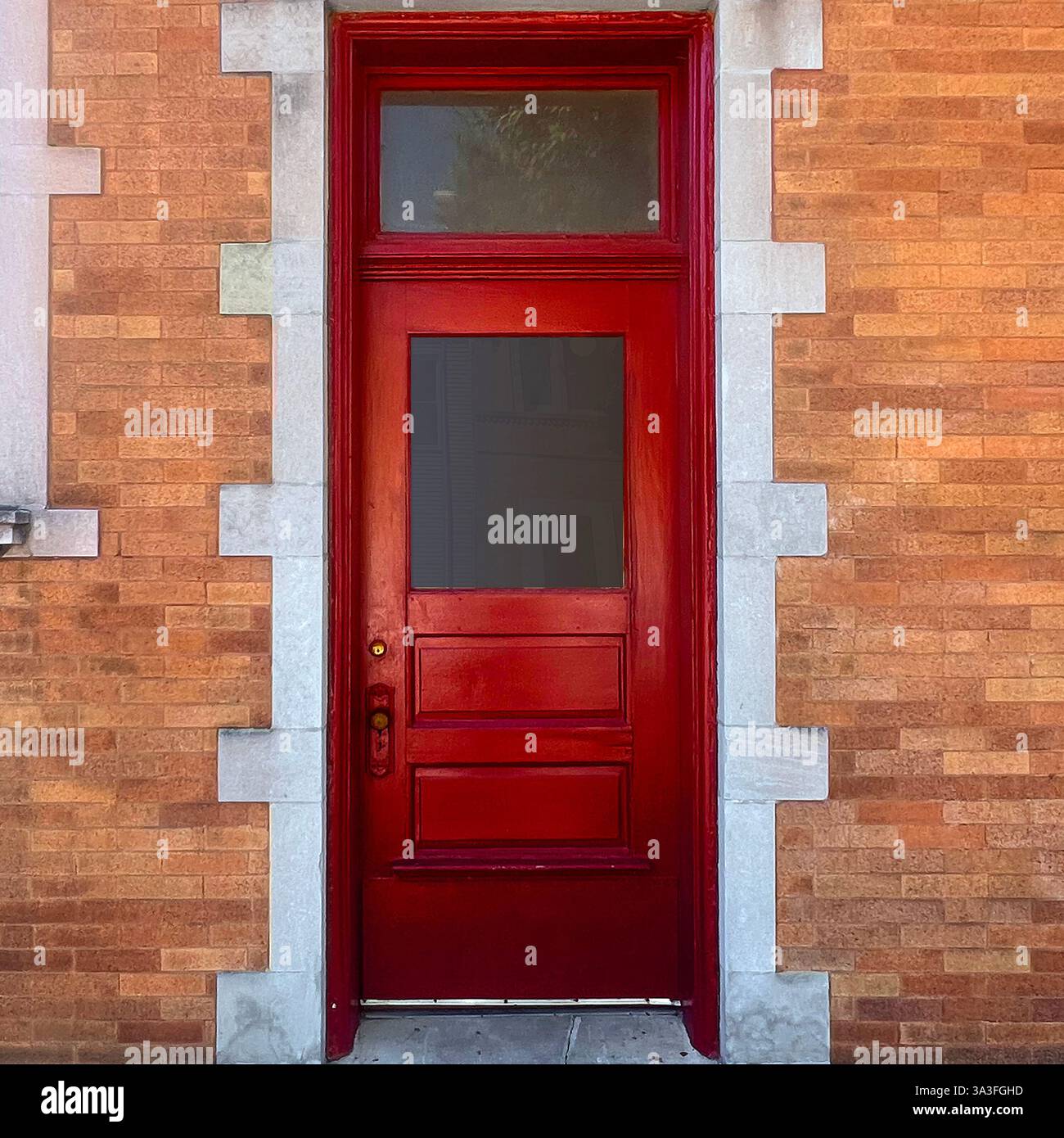 Red wooden door with transom window, set into an orange brick wall accented by decorative stone trim in Chicago. - Smartphone Captured Stock Image