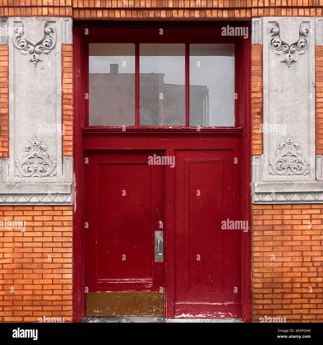 Red vintage door and transom window surrounded by ornate stone carvings and vibrant orange brick facade in Chicago. - Smartphone Captured Stock Image