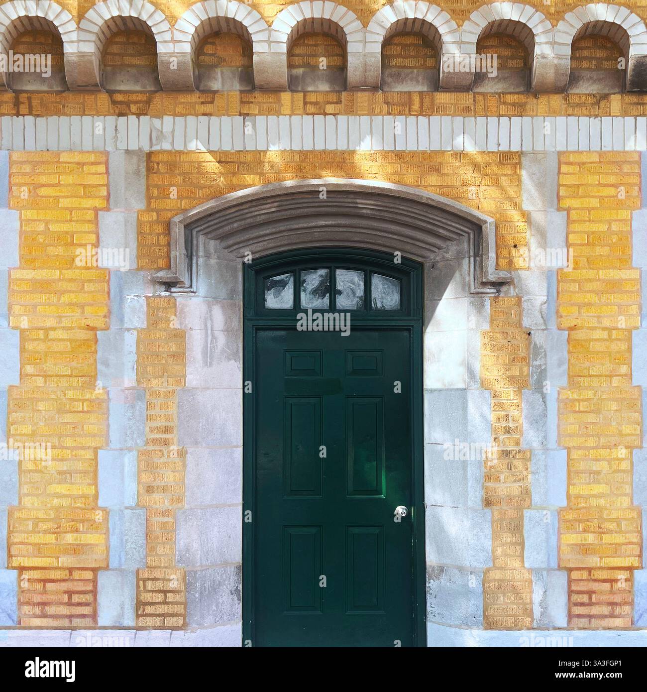 Dark greendoor with an arched transom window, set within stone archway, framed by a decorative yellow brick facade with intricate masonry detail. - Smartphone Captured Stock Image