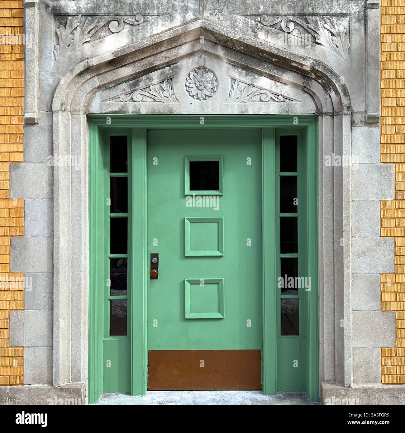 Gothic-style Mint green door, set within an ornate stone archway featuring floral carvings framed by a yellow brick facade, Chicago. - Smartphone Captured Stock Image