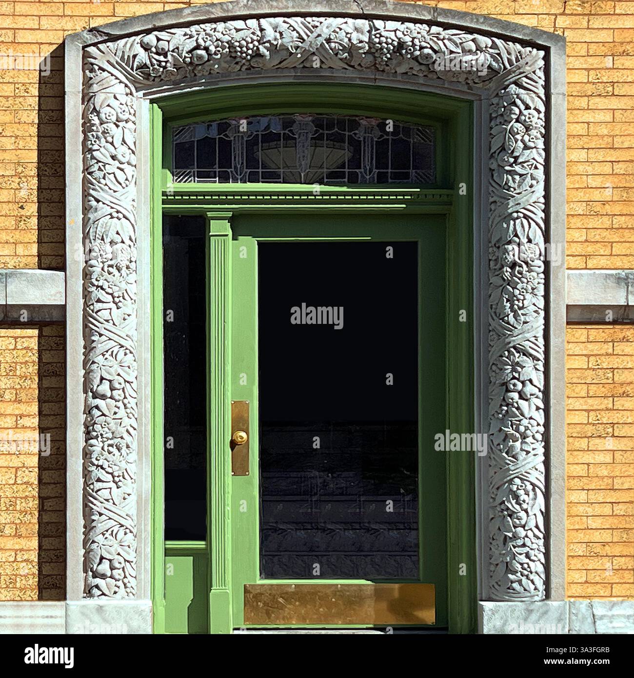 Green door framed by elaborate stone carvings and a decorative stained-glass transom, against a warm yellow brick facade. - Smartphone Captured Stock Image