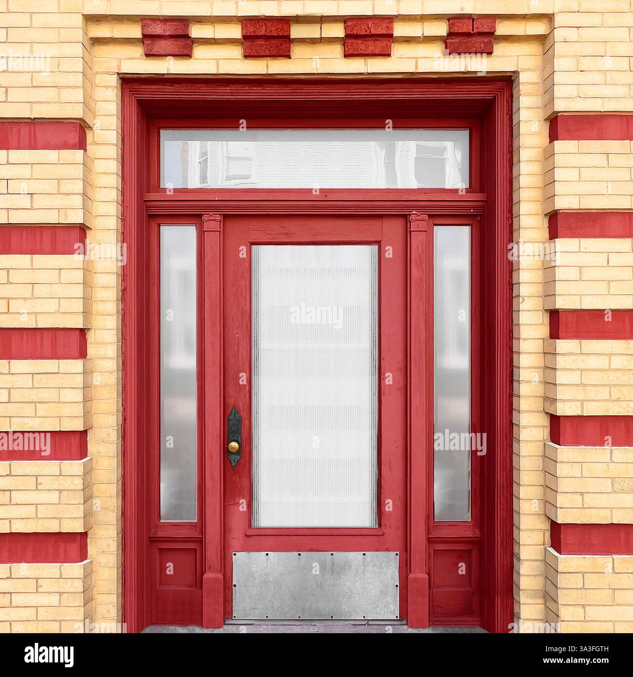 Red wooden door with frosted glass panels is framed by yellow and red striped brick pattern. - Smartphone Captured Stock Image