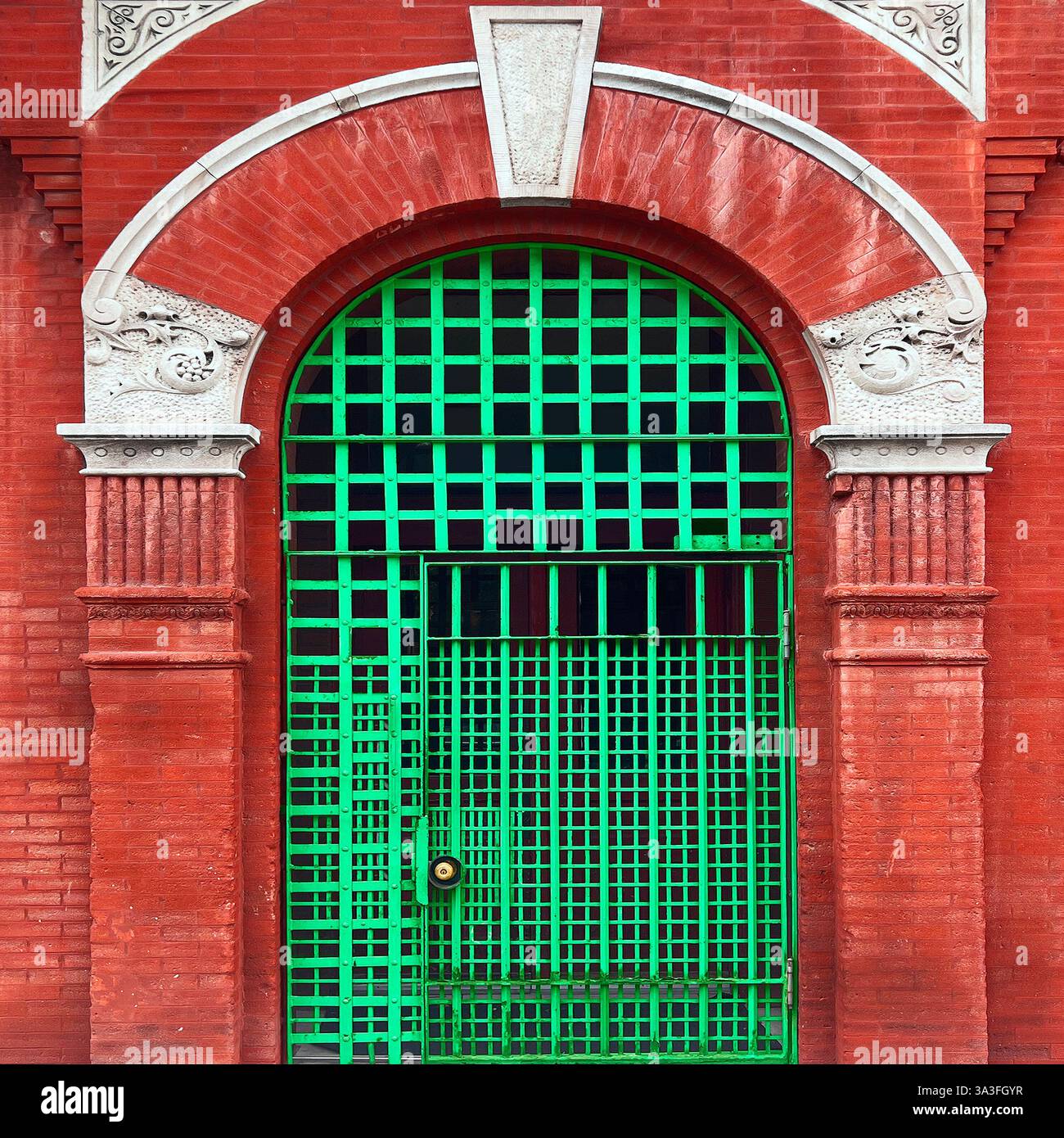 A vibrant green metal gate with a grid pattern set within a grand red brick archway, featuring ornate white stone details in Chicago - Smartphone Captured Stock Image