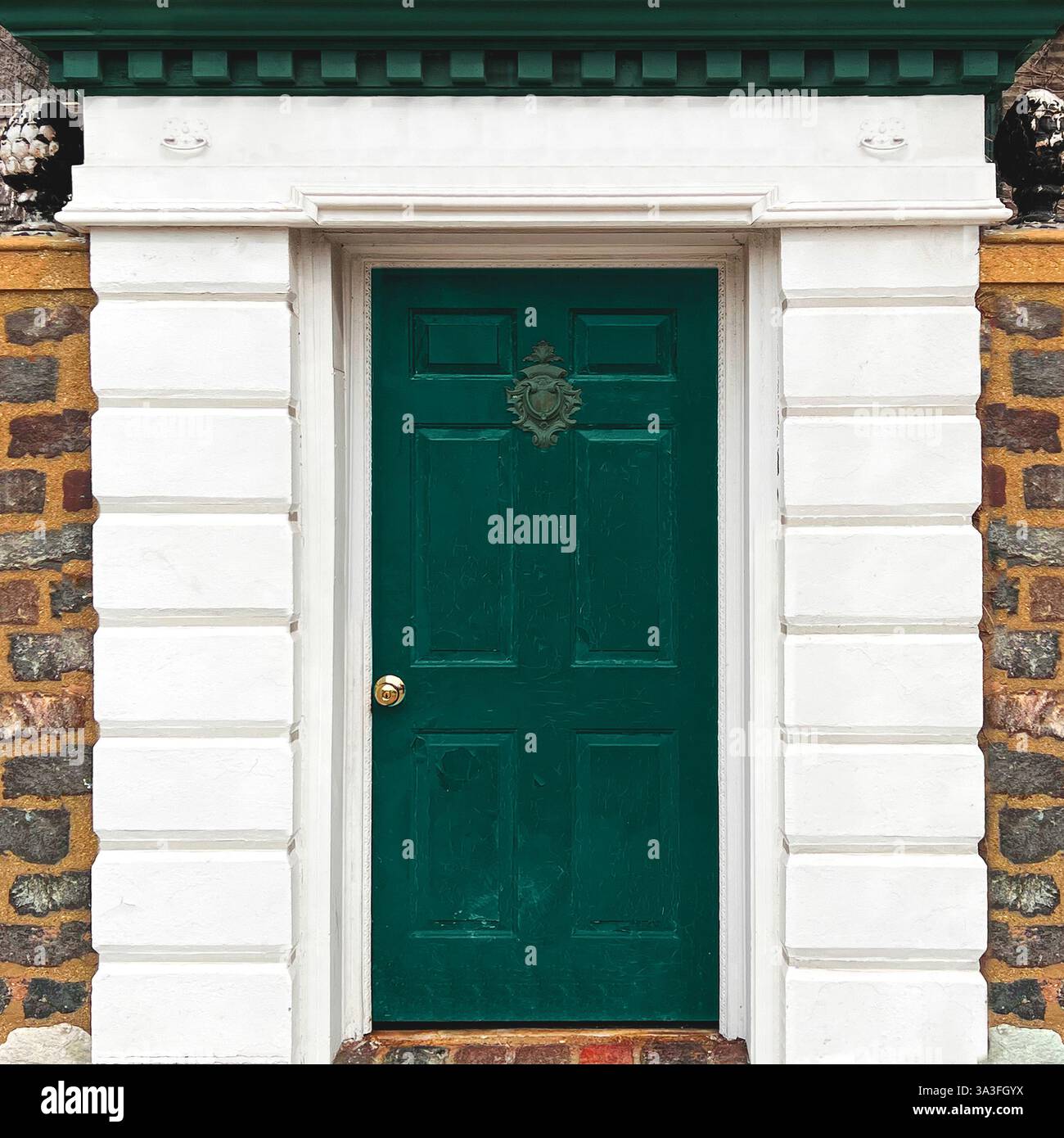 Green wooden door set within a white classical-style entrance, framed by a rustic stone wall, featuring an ornate door knocker in Chicago - Smartphone Captured Stock Image