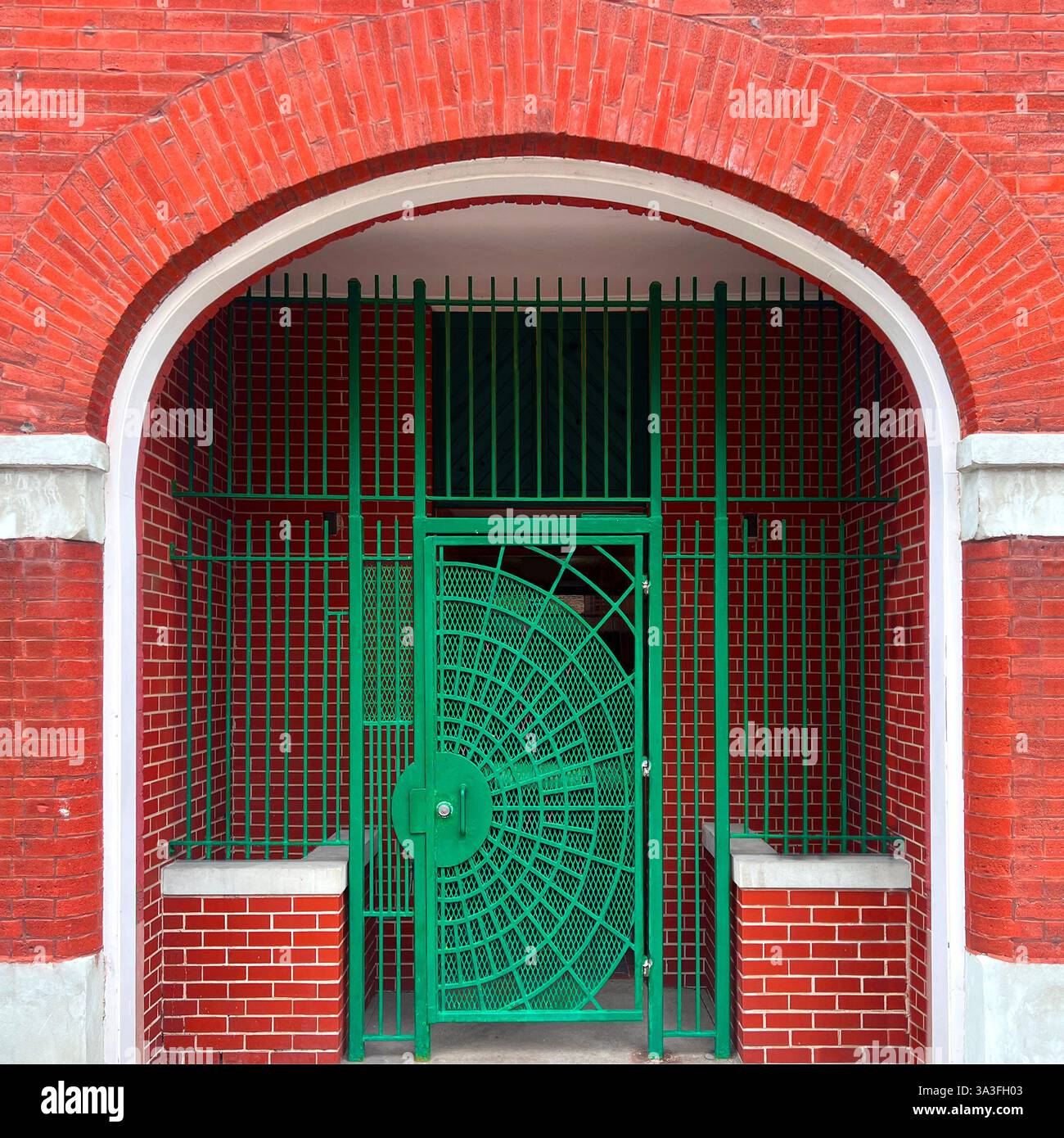Green metal gate with an intricate circular design, set within a red brick arched entryway in Chicago - Smartphone Captured Stock Image