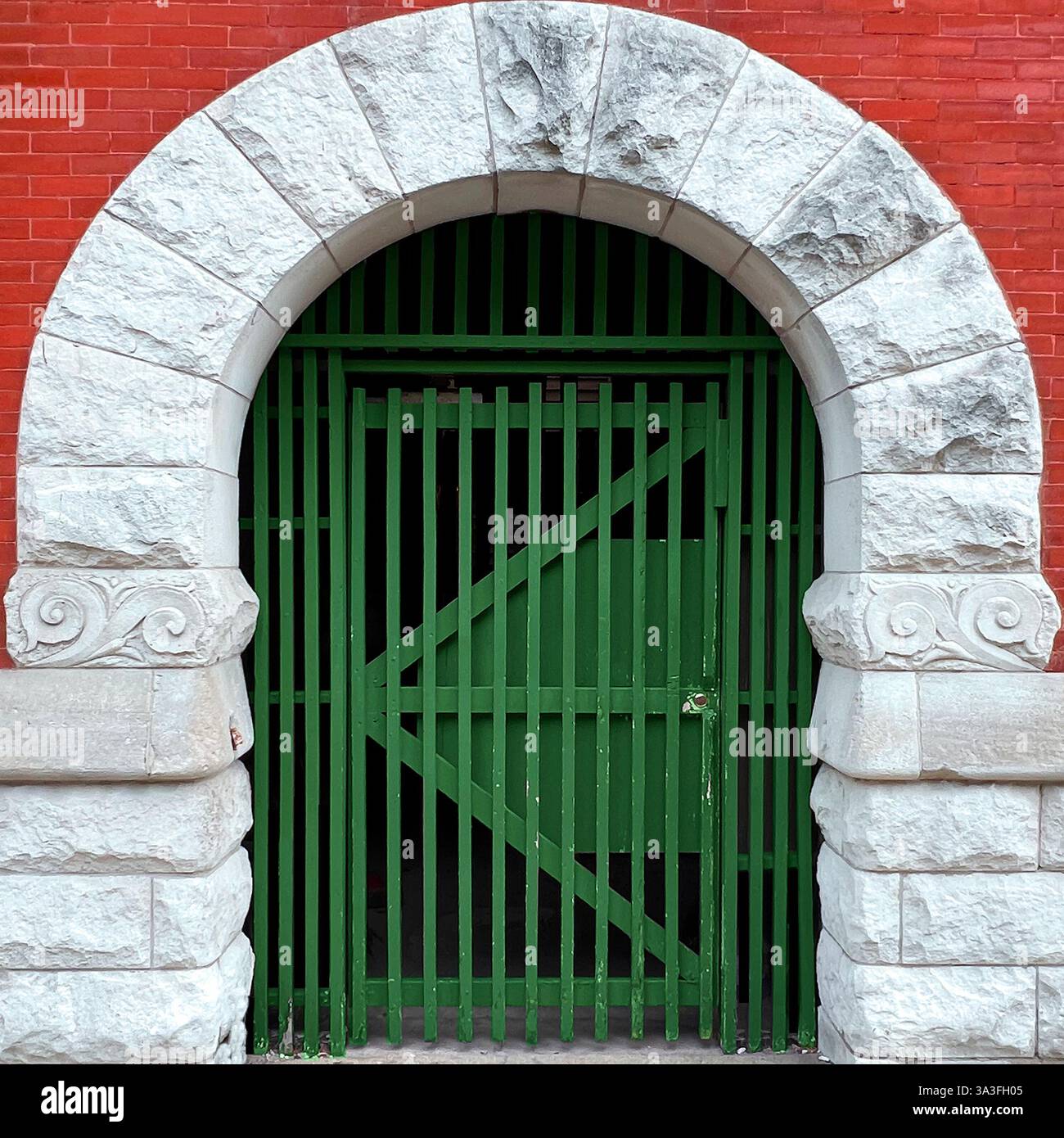 A green gated archway entrance with a wooden fence, framed by a historic stone and red brick structure in Chicago. - Smartphone Captured Stock Image
