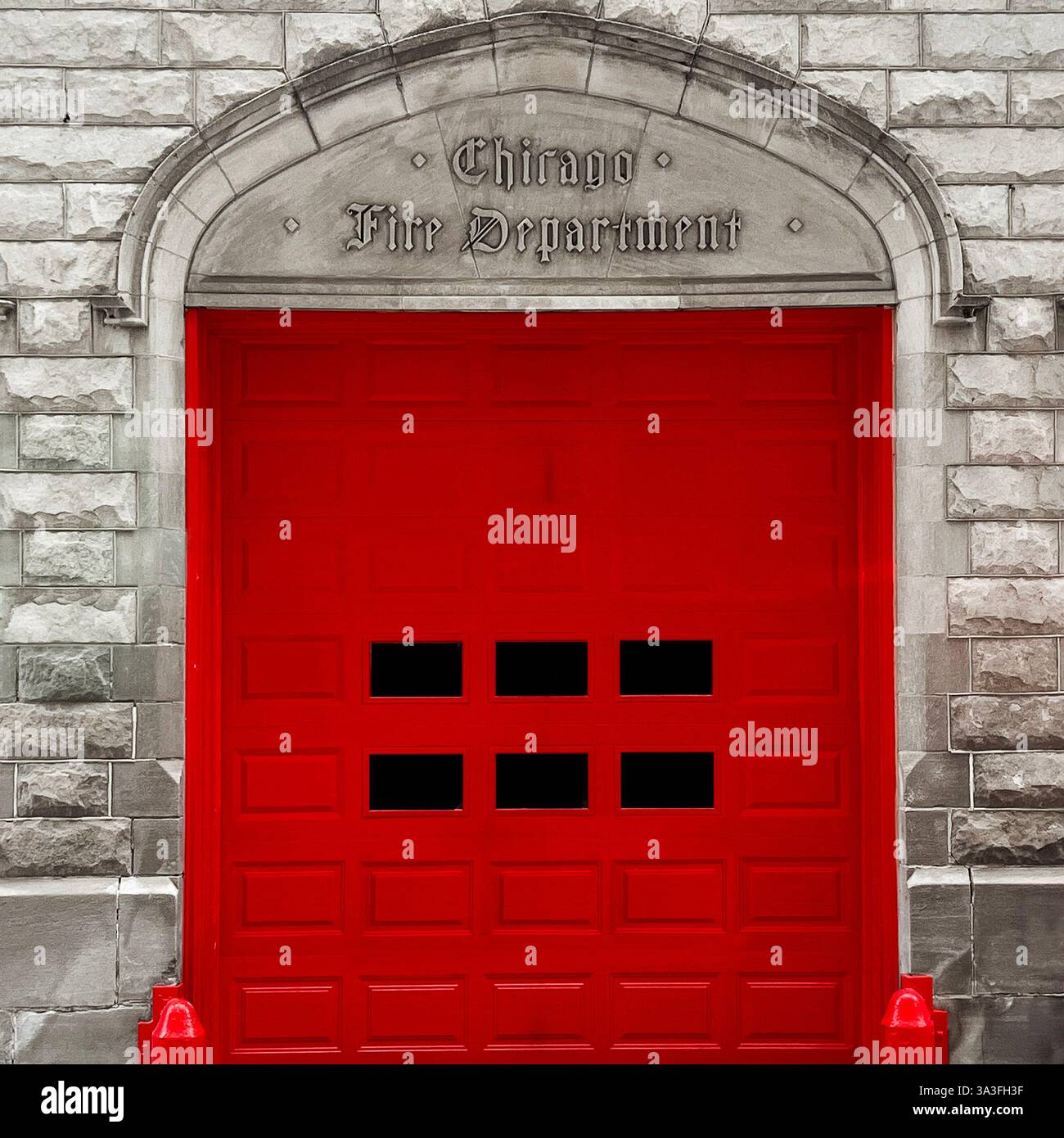 Red gate of a historic Chicago Fire Department, framed by an arched stone entrance with engraved lettering, set against a a classic stone facade - Smartphone Captured Stock Image