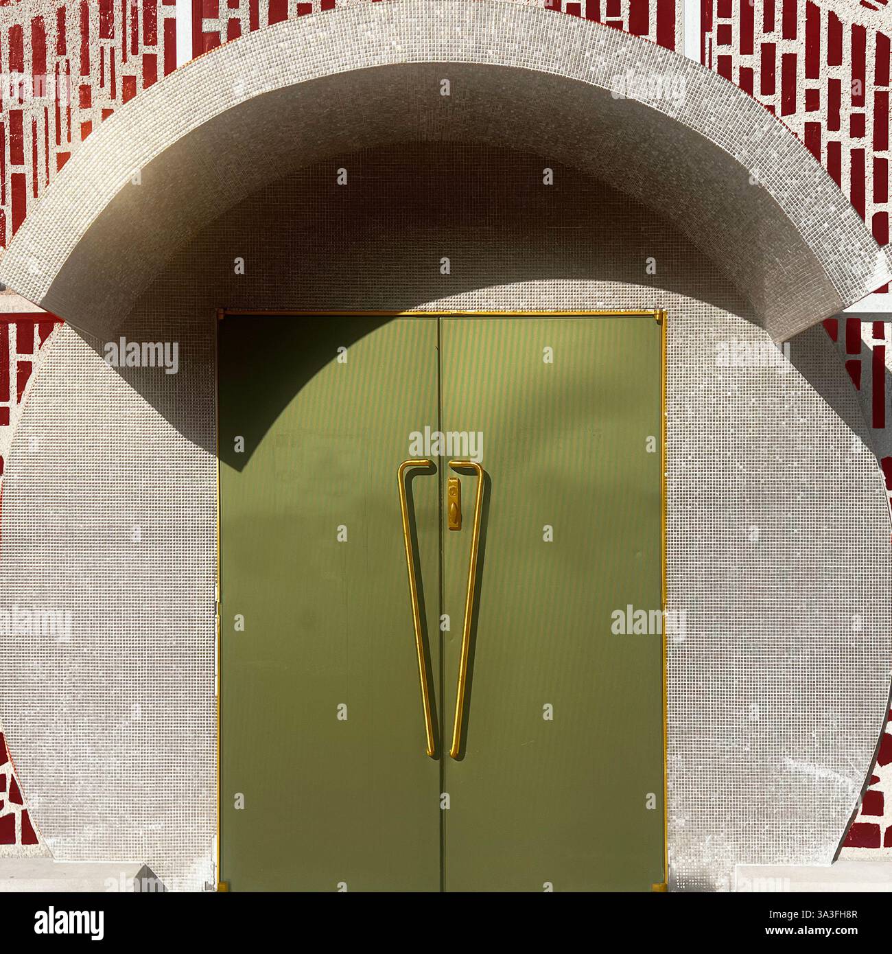 A  mid-century modern entrance with a green metal door framed by gold trim, set against a mosaic tile arch and geometric red patterned wall in Chicago. - Smartphone Captured Stock Image