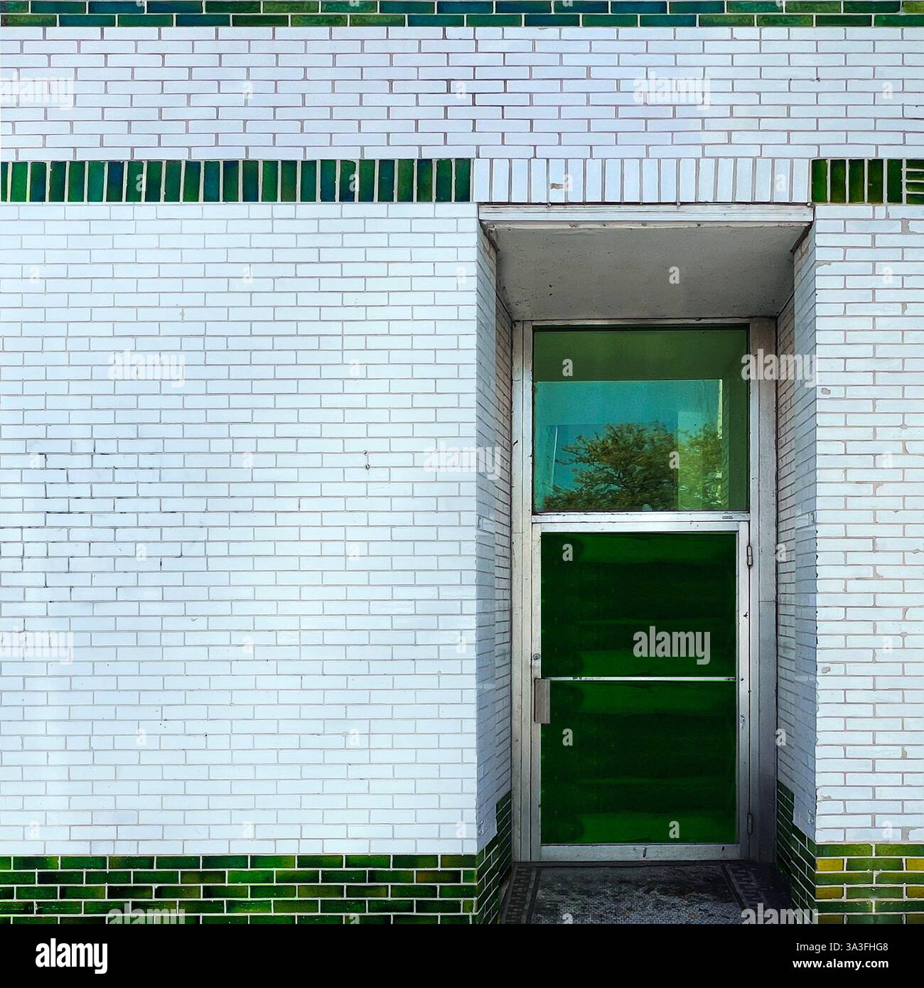 Green glass door set within a striking white and green-glazed brick facade, reflecting the surrounding in Chicago - Smartphone Captured Stock Image