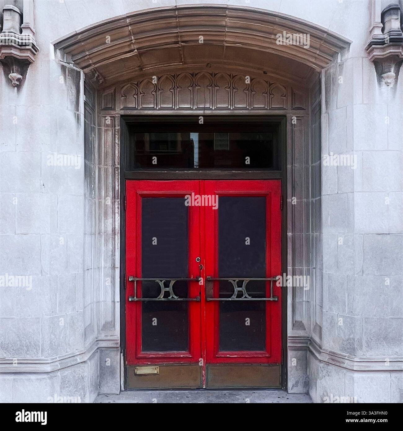 Red double door set within a grand Gothic-style stone archway, featuring intricate tracery and historic architectural details - Smartphone Captured Stock Image