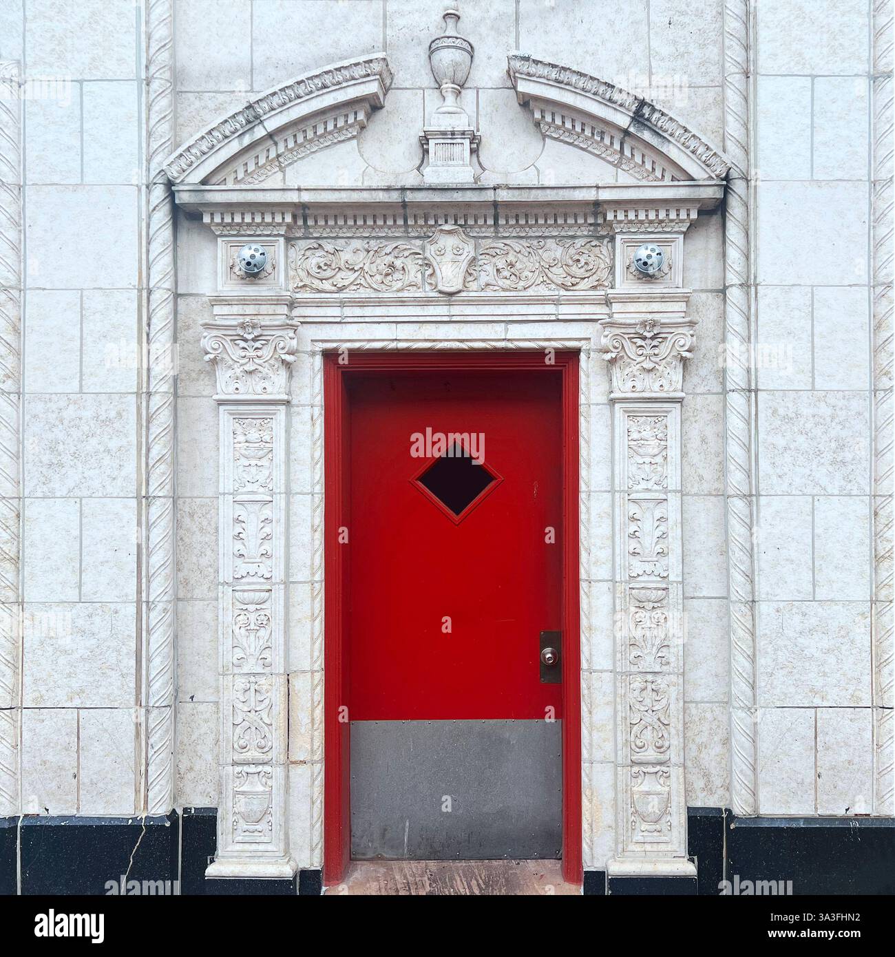 An ornate white stone facade frames a bold red door with a diamond-shaped window, showcasing intricate architectural details in Chicago - Smartphone Captured Stock Image