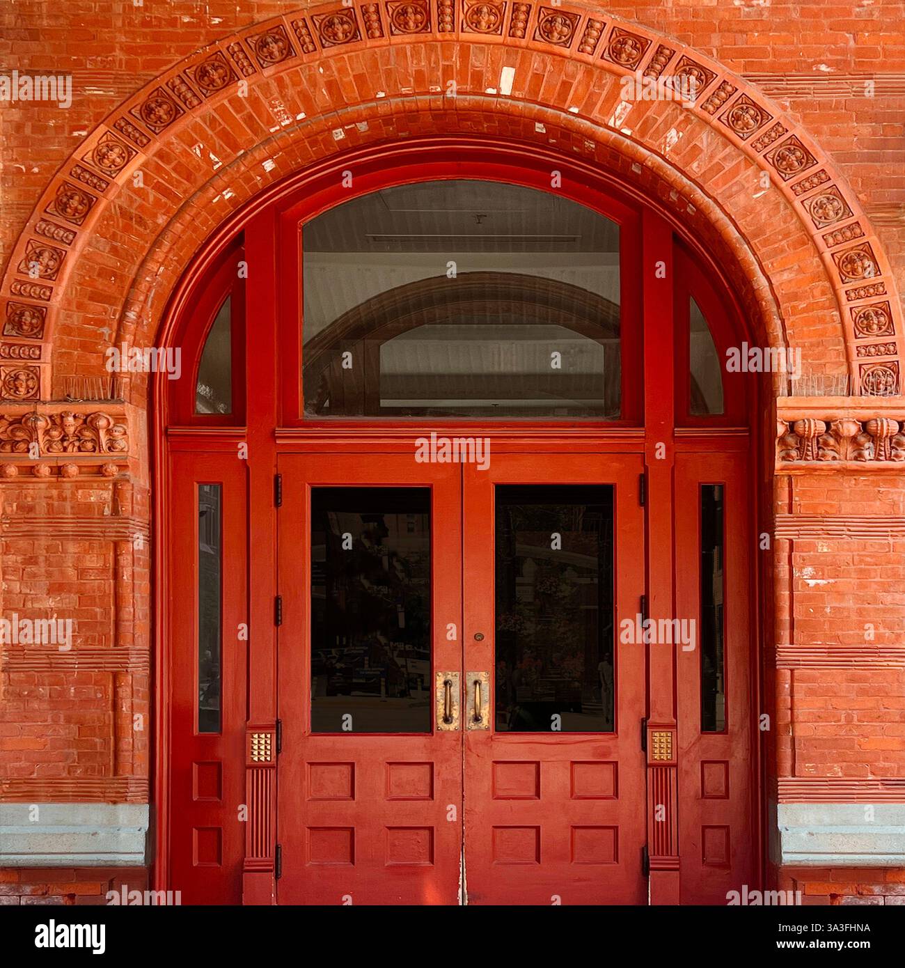 A grand red double door within an arched brick entryway, adorned with intricate terracotta detailing in Chicago - Smartphone Captured Stock Image