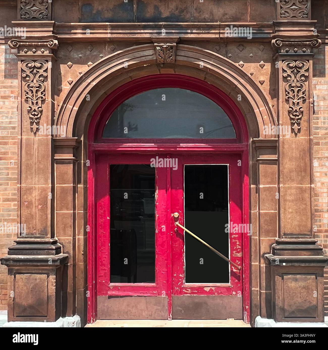 Red door featuring ornate carved details and glass panel accents, set within an intricately patterned stone archway and brick facade in Chicago - Smartphone Captured Stock Image