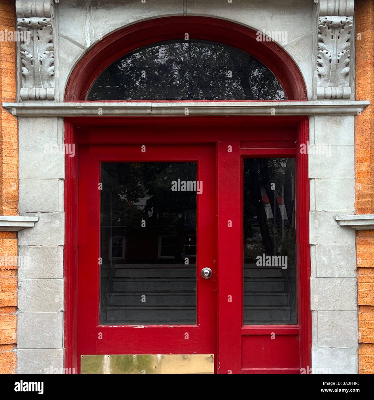 Vintage red wooden door with glass panels and an arched transom window, framed by decorative stone detailing on a historic brick building. - Smartphone Captured Stock Image