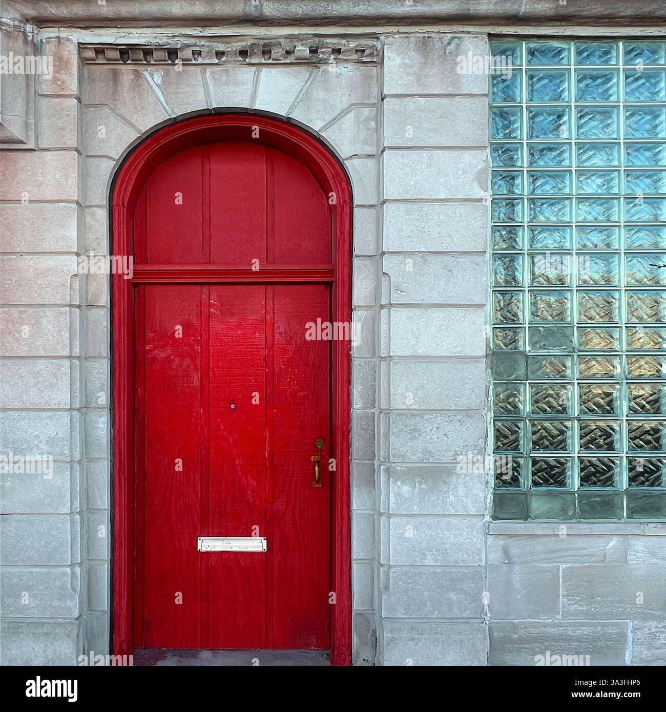 Striking red arched door set in a stone facade beside a vintage glass block window in Chicago’s urban landscape - Smartphone Captured Stock Image