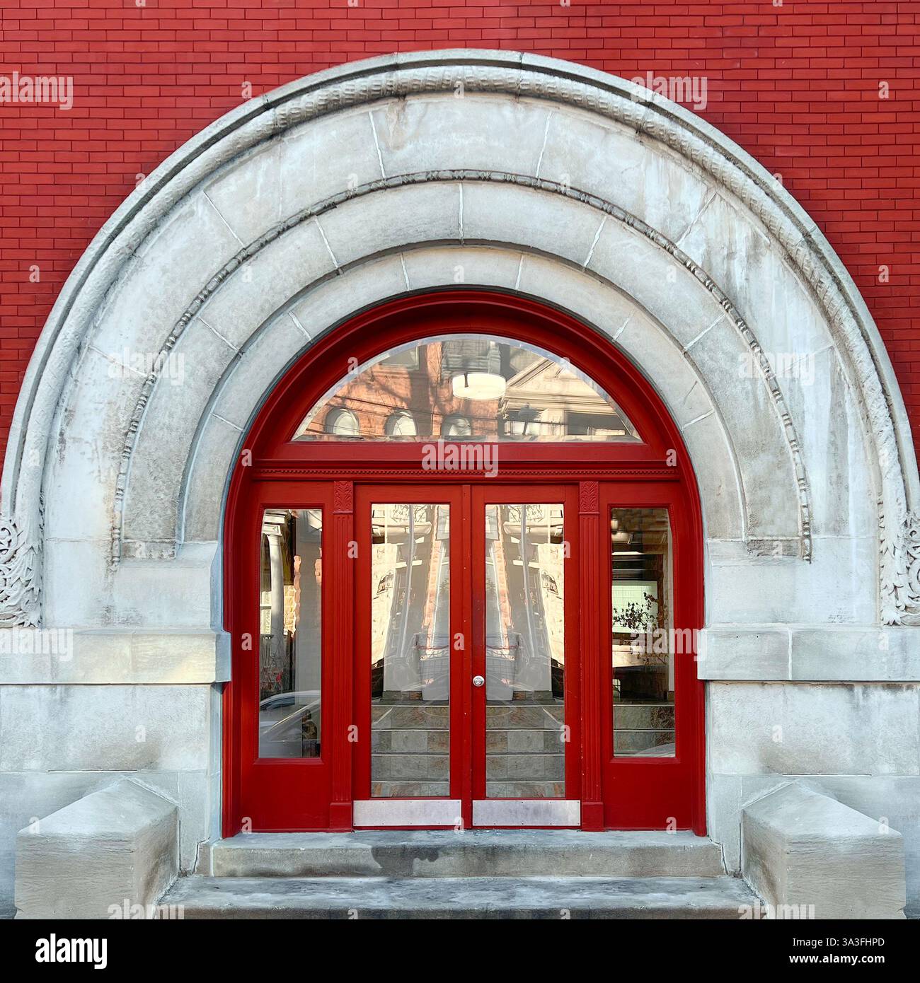 A striking arched red double door entrance framed by a grand limestone archway, set against a red brick facade. - Smartphone Captured Stock Image
