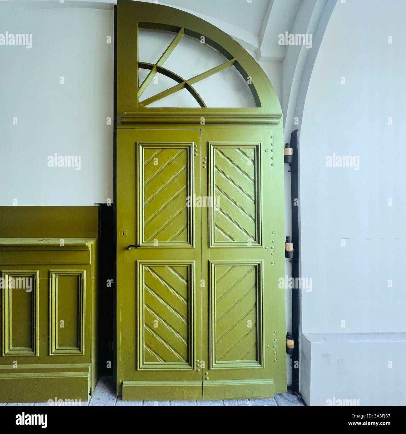 An elegant olive-green wooden door with an arched transom window and intricate paneling enhances the historic interior of a building in Łódź, Poland - Smartphone Captured Stock Image