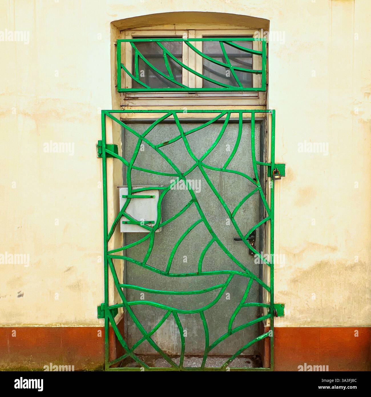 A creatively designed green metal security gate with an abstract, wavy pattern guards an old industrial entrance in Łódź, Poland - Smartphone Captured Stock Image