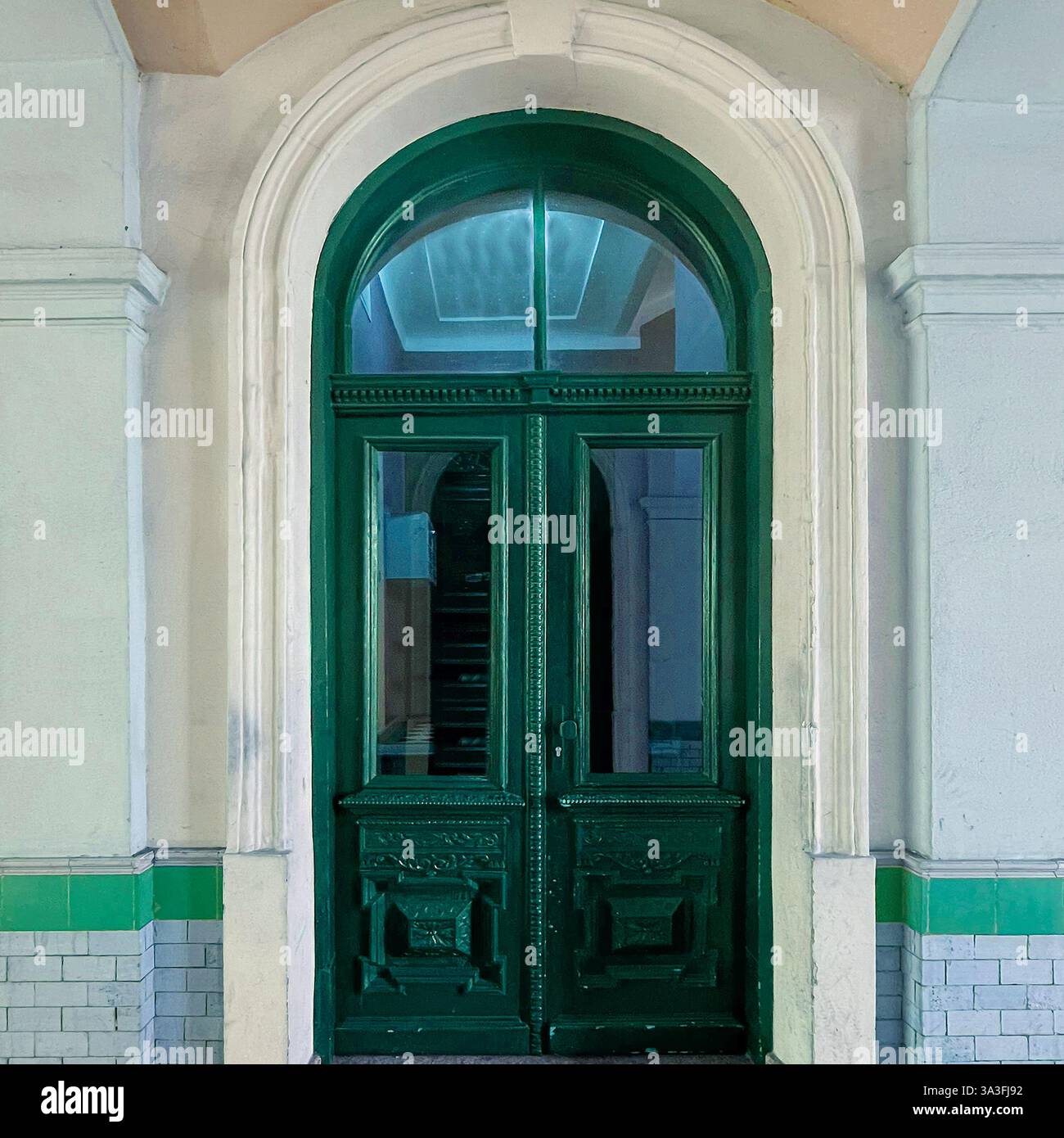 An elegant dark green arched doorway with intricate carvings and glass panels, set in a historic Warsaw building - Smartphone Captured Stock Image