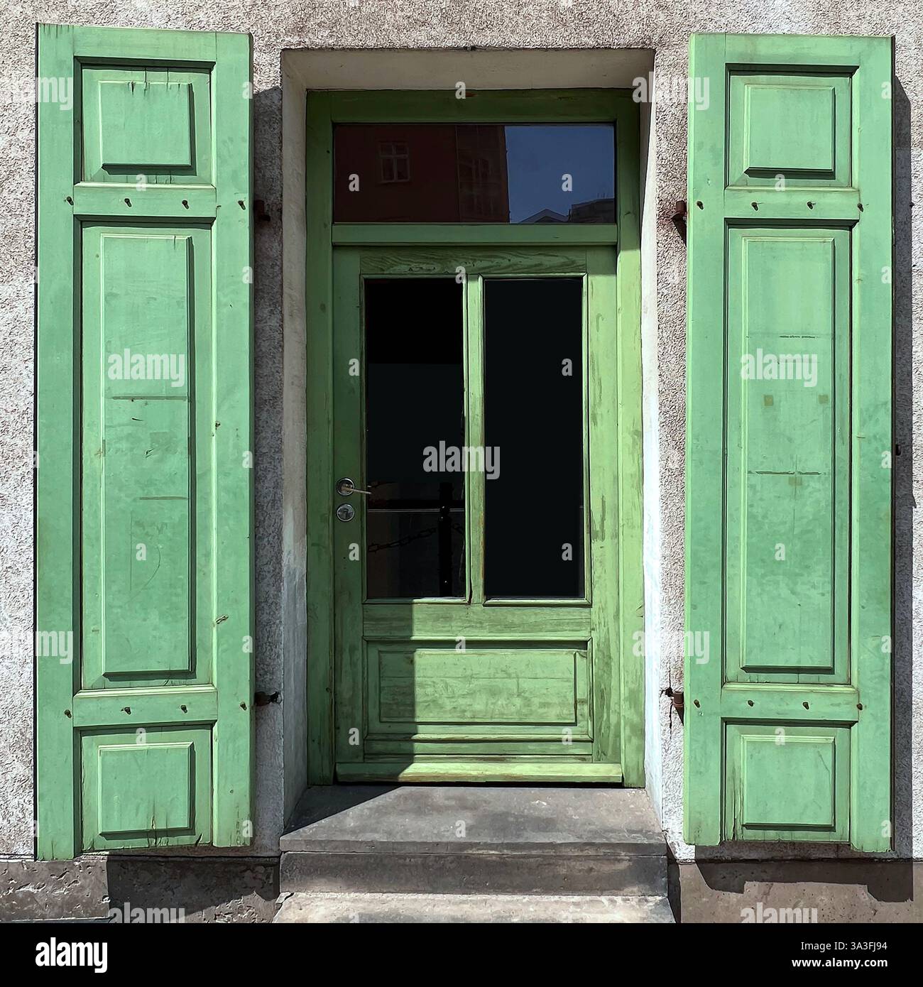 A vintage green wooden door with open shutters, revealing a dark interior, in the heart of Warsaw, Poland - Smartphone Captured Stock Image