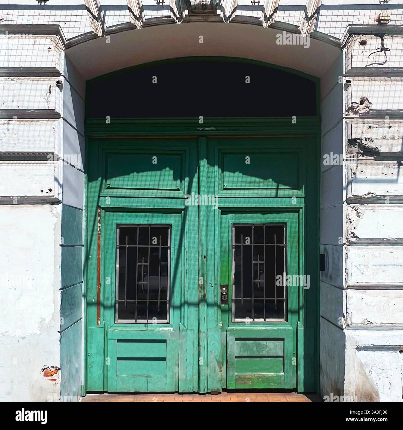 A weathered green wooden gate with barred windows set in an old historic building in Warsaw, Poland - Smartphone Captured Stock Image