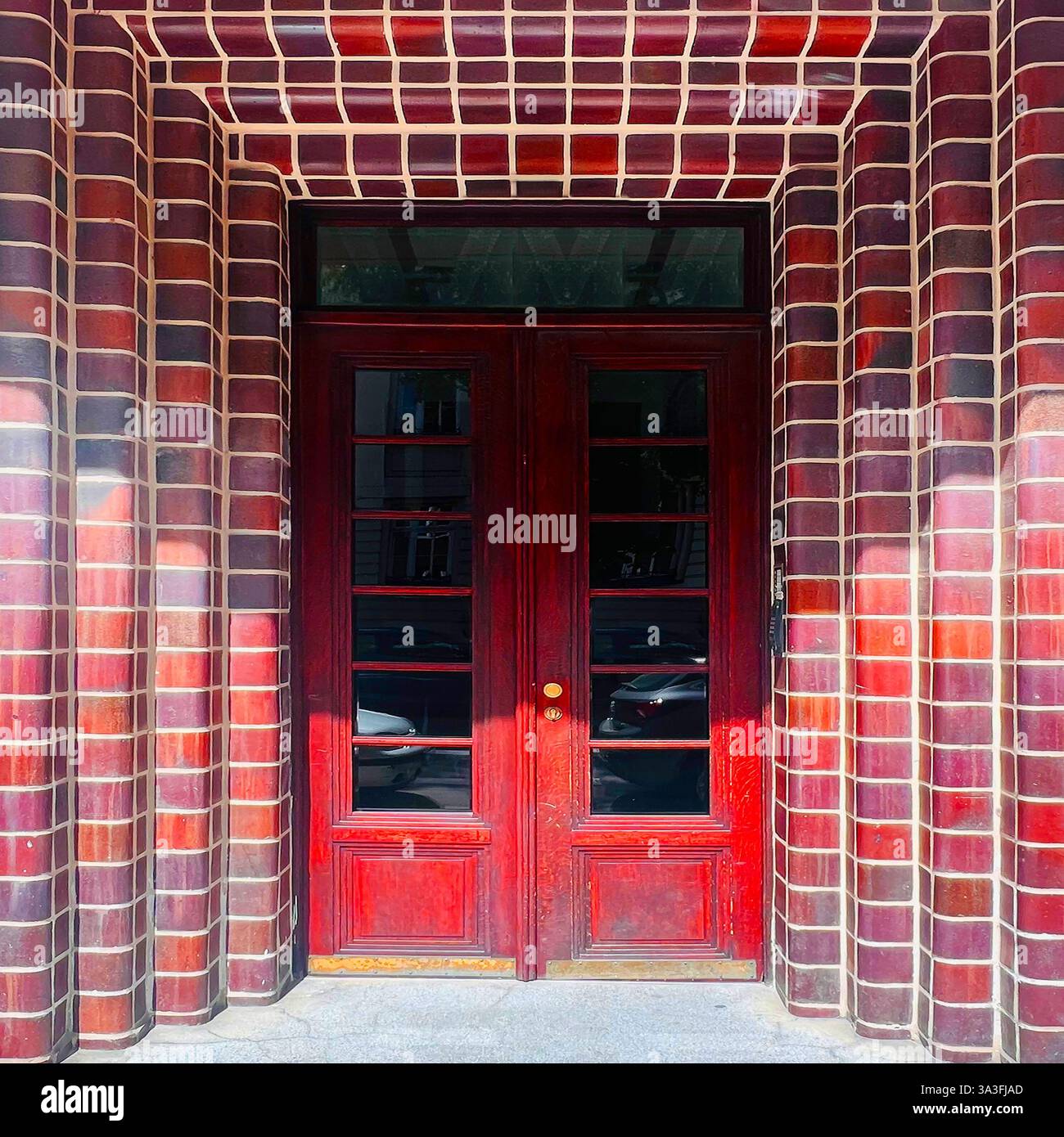 Modernist double doors in Krakow, Poland, framed by deep red glazed brickwork with curved geometric detailing, style of early 20th-century modernism - Smartphone Captured Stock Image