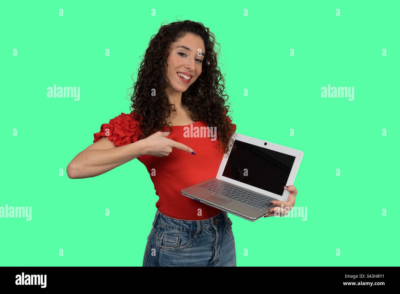 Smiling woman pointing at laptop with blank screen on green background, ideal for mockups and presentations Stock Photo