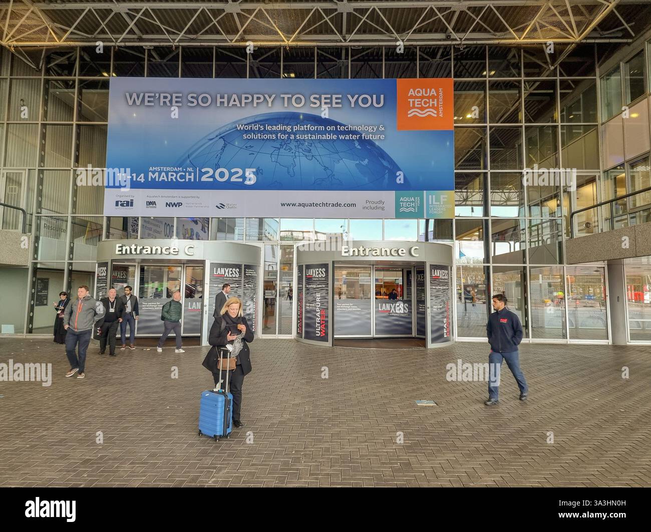 Main entrance to Aquatech fair 2025 in Amsterdam RAI, The Netherlands, Europe with big poster 'We're so happy to see you'; person with trolley - Smartphone Captured Stock Image