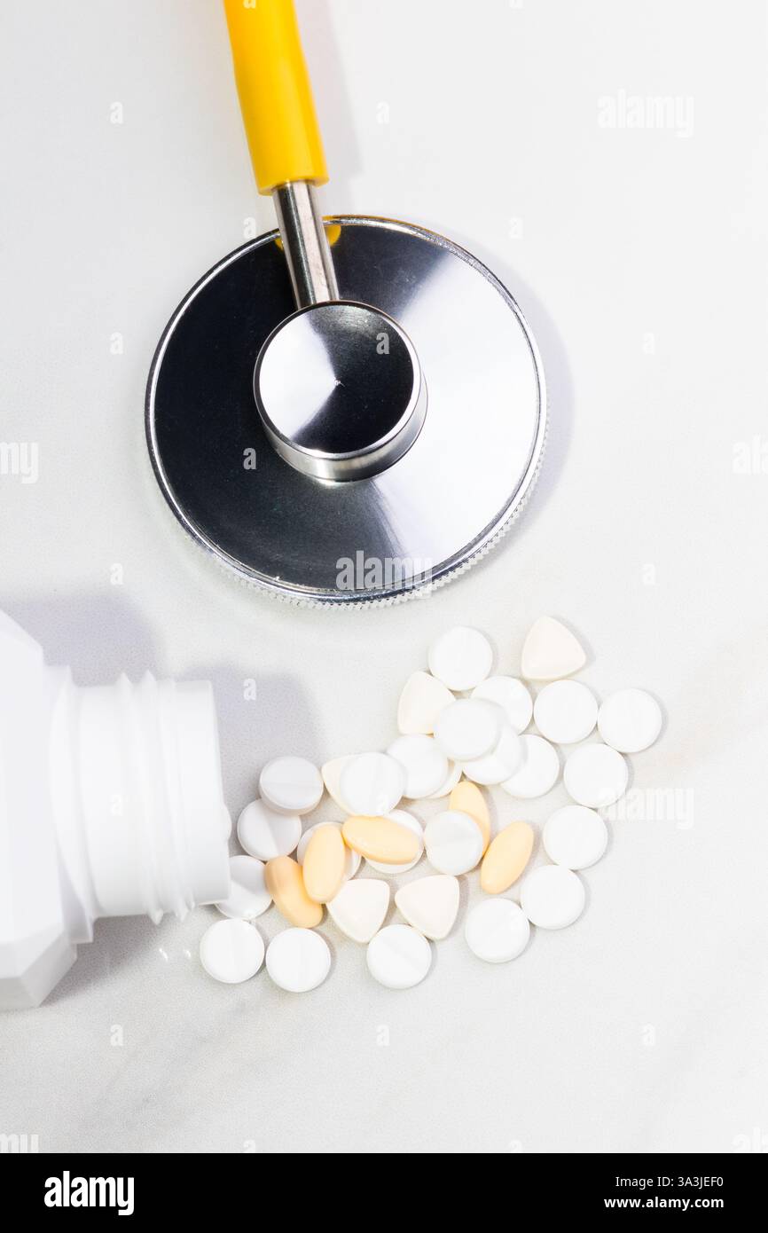 Close-up image of various white and beige medical pills scattered on a reflective surface, accompanied by a stethoscope. The image conveys themes of h Stock Photo