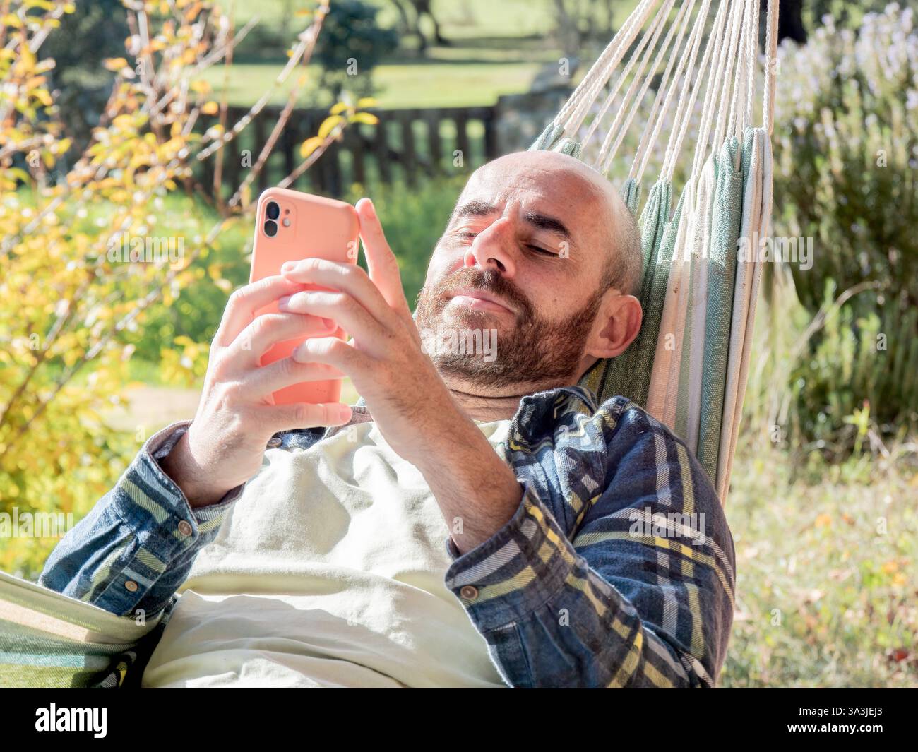 Man relaxing in hammock using smartphone outdoors Stock Photo