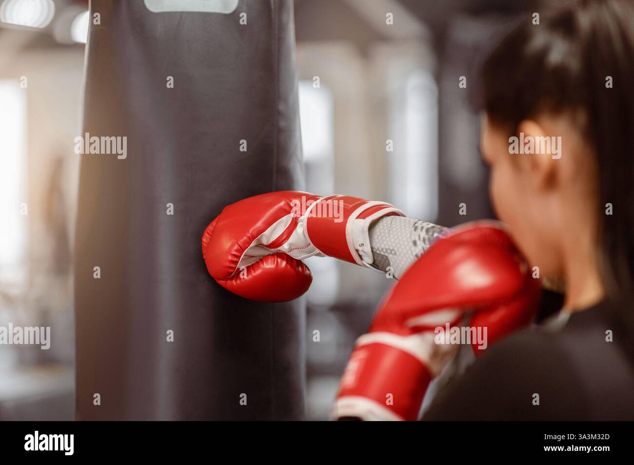 A woman practices boxing techniques on a punching bag in a gym setting Stock Photo