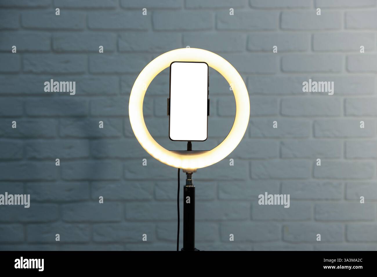 Ring lamp with smartphone against brick wall Stock Photo