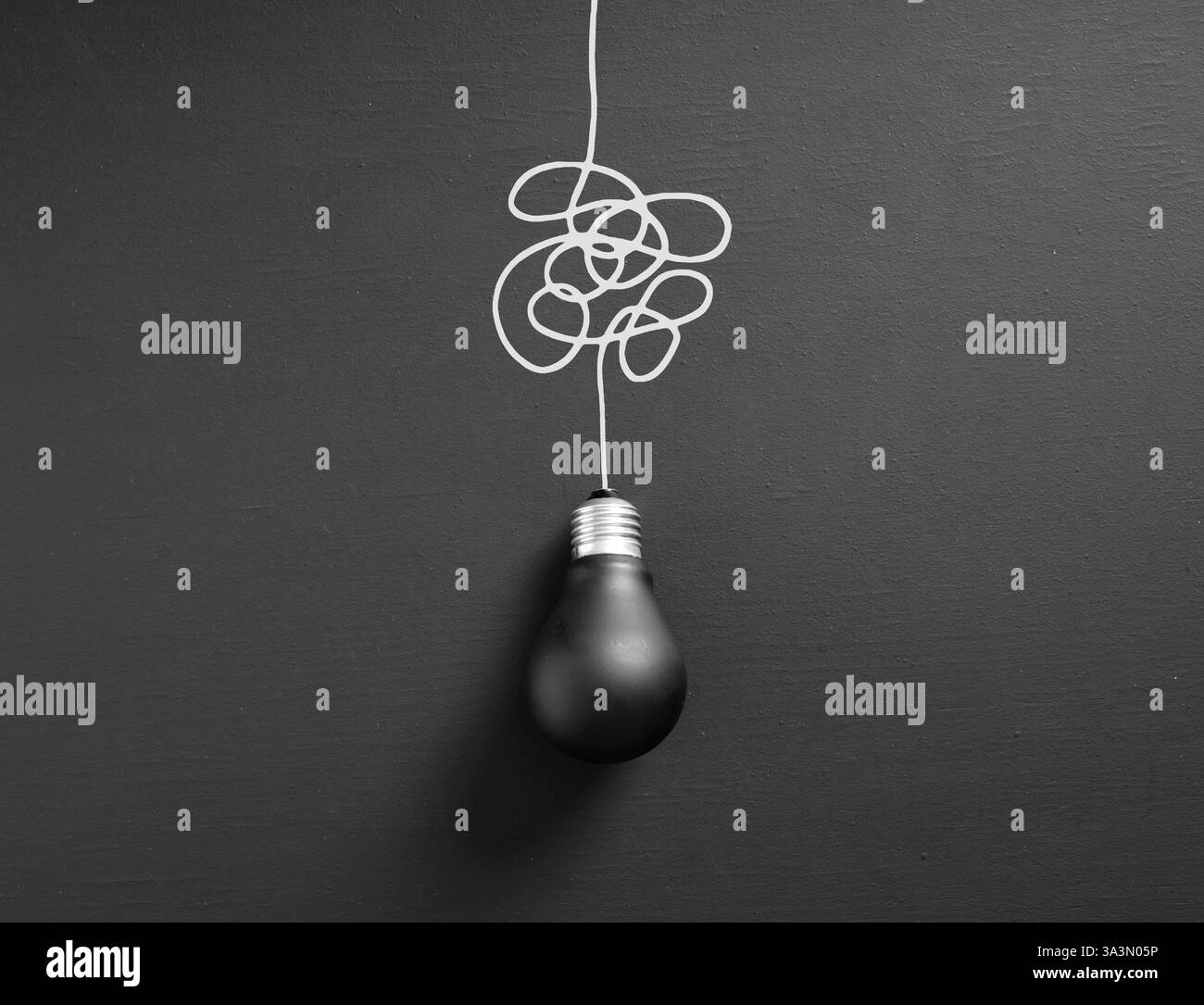 Black light bulb hanging from a tangled white cable on a dark background, representing the concept of confusion and lack of ideas Stock Photo