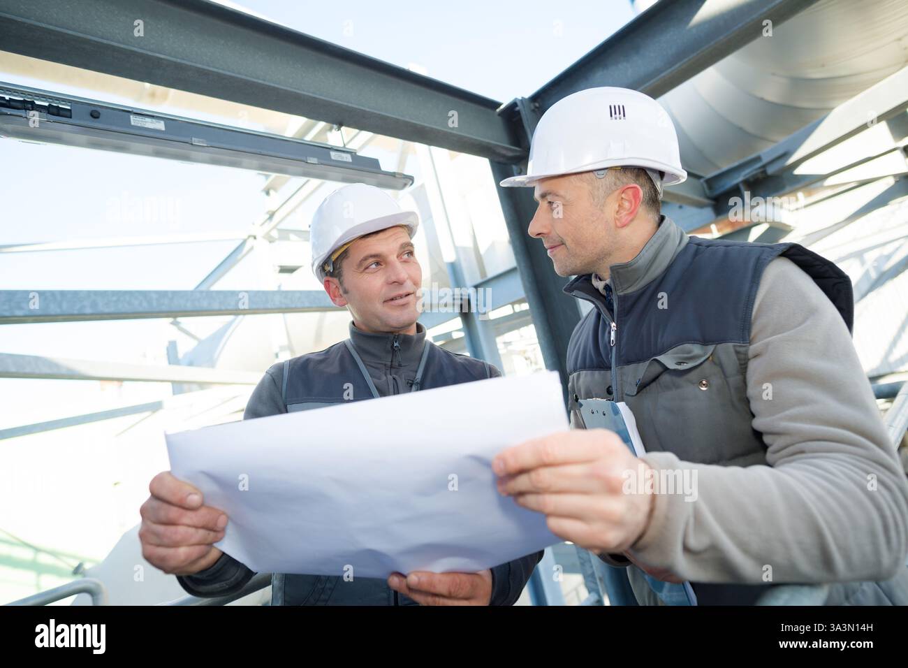 supervisor with workers examining blueprints at table in industry Stock Photo
