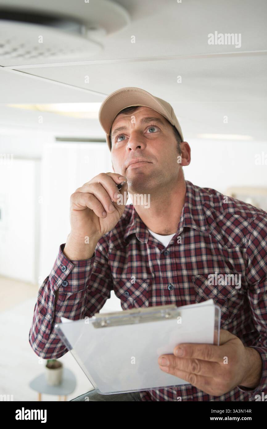 male technician looking at smoke detector and taking notes Stock Photo